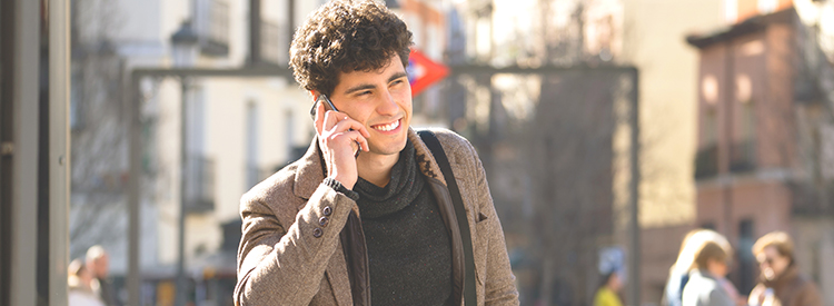 Young attractive happy man talking on smart phone in european city Young attractive man in his twenties happy talking and chatting with friend on social media on smart phone on holidays in europe. In communication, technology internet and lifestyle concept.